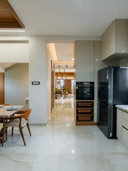 An open-plan kitchen and dining area where traditional and modern elements meet. The kitchen features sleek, handle-less cabinets, while the dining area is defined by a traditional wooden pillar and a marble-top table.