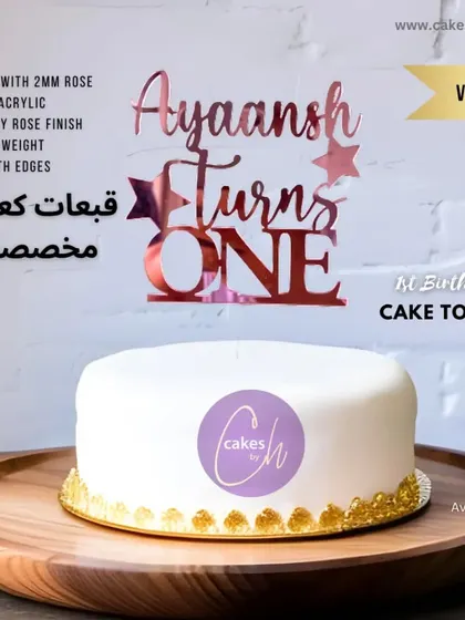 A "Ayaansh Turns ONE" topper crafted from beautiful rose gold acrylic. The modern script font and star details make it a stylish choice for a baby boy's first birthday cake.