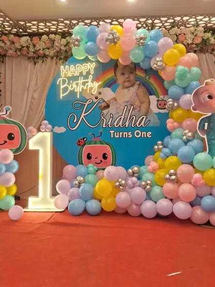 A beautiful Cocomelon themed decoration for Kridha's first birthday. The setup includes a custom backdrop with her photo, a pastel balloon arch, and a light-up number '1'.