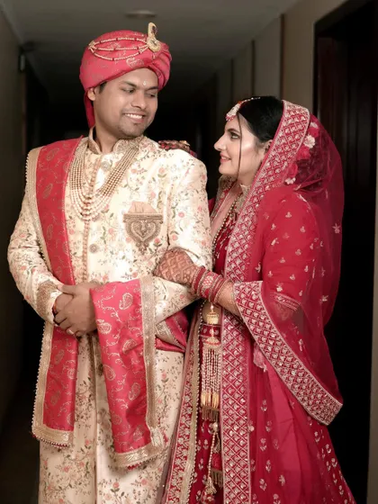 A sweet, candid moment between the bride and groom. Their matching red and cream outfits are beautifully coordinated, and their loving gaze says it all.