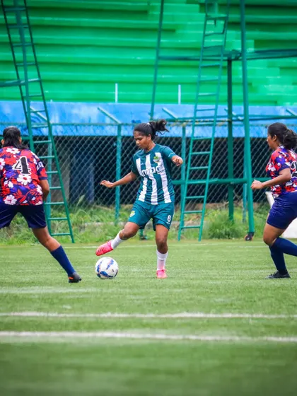 A player in our green and white striped kit skillfully controls the ball while being closed down by two opponents.
