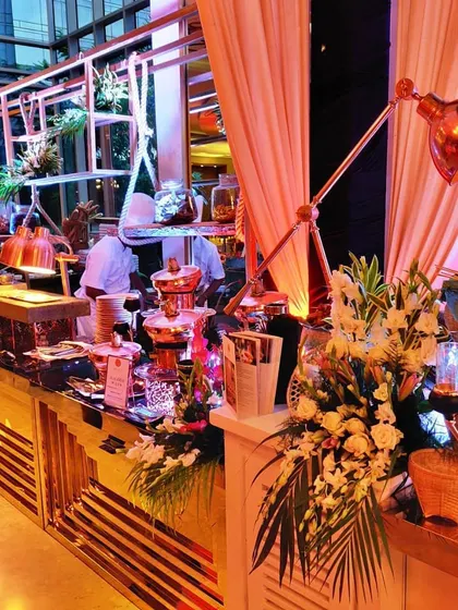 A stylish and contemporary buffet counter at a hotel event. The combination of warm lighting, fresh flowers, and our professional chefs in the background showcases a seamless and high-quality catering operation.