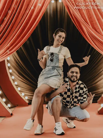 A fun and energetic pose on a 'red carpet' set with stage lights, capturing the couple's playful and star-like quality.