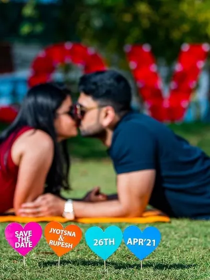 A fun picnic-style pre-wedding shoot in a park. The "LOVE" sign in the background and the custom "Save the Date" hearts make this a personalized and sweet memory.