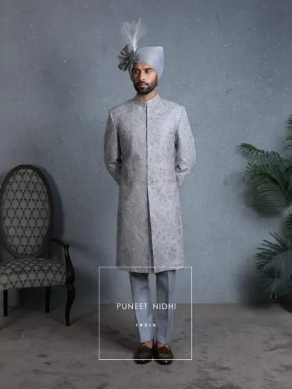 A powder blue wedding sherwani inspired by Mughal architecture, adorned with intricate zari embroidery in silver and gold threads, weaving paisley and floral artistry into every fold.