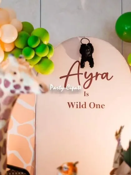 A life-sized giraffe prop next to the 'Ayra is Wild One' backdrop. Using large props like this really helps in creating an immersive and impressive party environment.