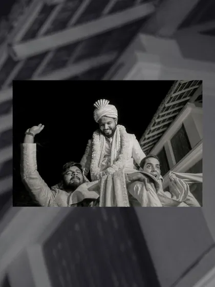 The groom being lifted onto his friends' shoulders during the baraat, a classic moment of celebration captured in a dramatic black and white photo.