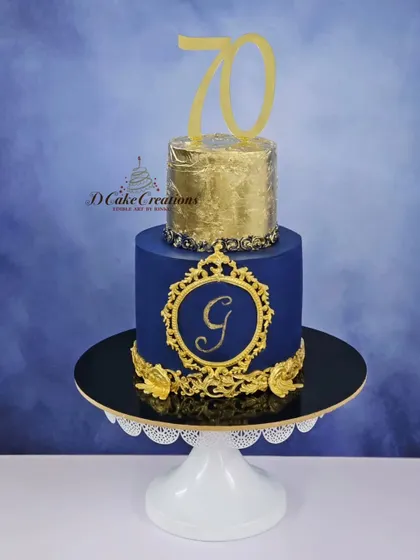 A regal cake for a 70th birthday celebration. This two-tier cake in royal blue and gold features a monogram, intricate baroque details, and a top tier covered in edible gold leaf.