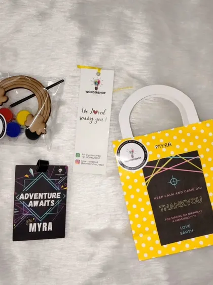 A complete return gift set for a laser tag party. It includes a personalized "Adventure Awaits" tag and a rainbow craft kit, all packed in a cheerful bag with a custom thank you note.