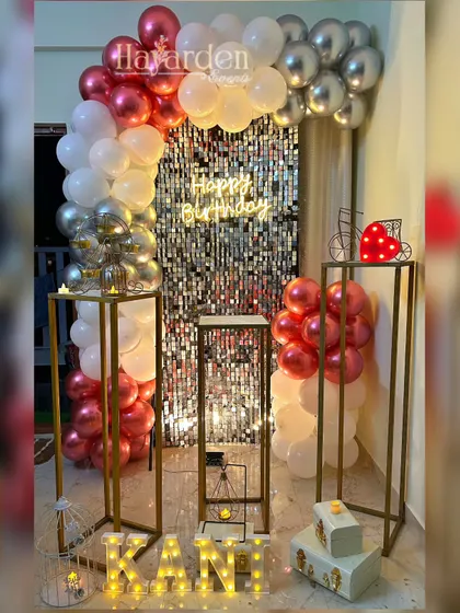 An elegant home party setup with a silver sequin backdrop and a balloon arch in metallic red and silver. The tall pedestals and marquee letters add a touch of class.