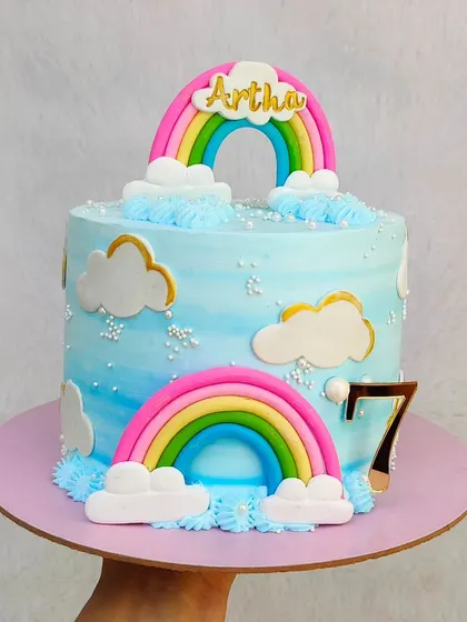 A dreamy rainbow and clouds cake for a 7th birthday. The soft blue buttercream is decorated with fluffy buttercream clouds and fondant rainbows.
