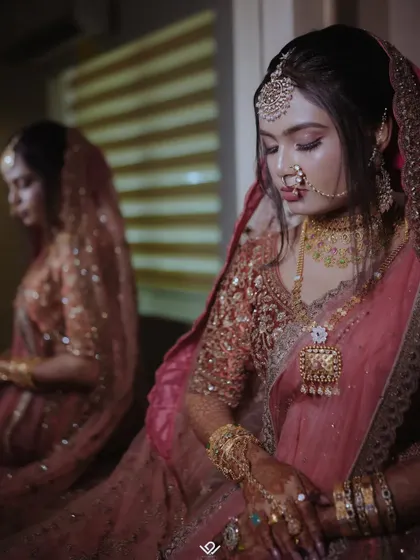 A bride in a pink lehenga looks down, her reflection captured in the surface beside her, creating a thoughtful and artistic image.