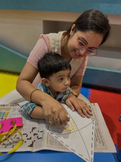 A mother and son are focused on decorating a paper kite, an activity that requires precision and develops fine motor skills.