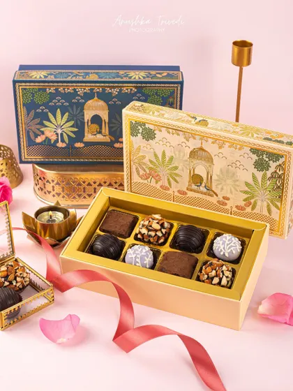 A luxurious shot of ornate blue and gold chocolate boxes for Diwali, with rose petals and brass decor adding to the elegance.