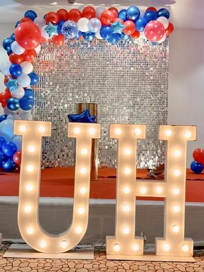 A simple and elegant stage setup with a silver shimmer wall and large marquee letters spelling "RUHI".