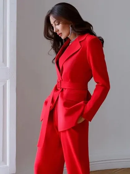 A bold red pant suit designed with a self-tie belt for a defined waist. This small detail transforms the silhouette, offering a different way to wear a classic blazer.