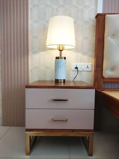 A detail shot of the bedside table with its elegant lamp, pink drawers, and gold-finished metal base, perfectly complementing the room's color scheme.