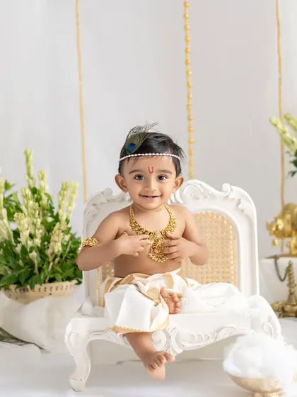 A little Krishna sitting regally on a miniature white throne. The elegant setup with white and gold accents makes this a truly special portrait for Janmashtami.