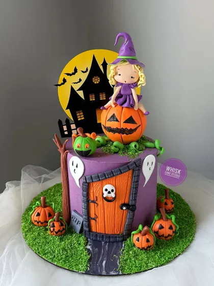 Halloween is here with this witch-themed cake. Perfect for a spooky celebration, it features a cute witch figurine sitting on a pumpkin in a haunted setting.