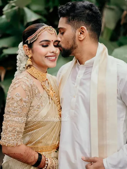 An intimate and sweet moment. The groom's simple white kurta and angavastram provide a clean canvas, making his bride, in her stunning gold-on-gold ensemble, the absolute center of attention.