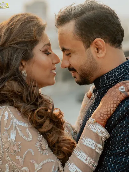 An intimate close-up from Dhwani and Riten's Sangeet night. The focus is on their connection, with her henna-adorned hand gently touching his shoulder.