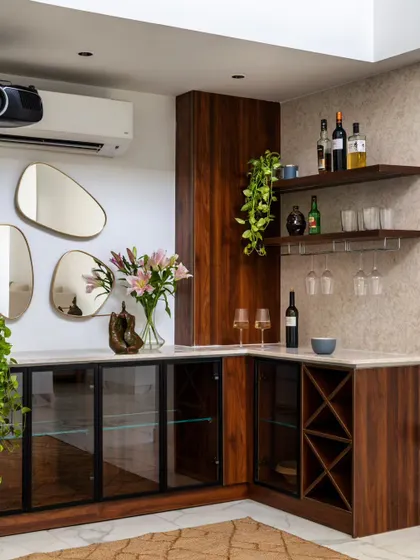 A bespoke home bar designed to blend luxury with function. The corner unit features dark wood cabinetry with glass doors, a built-in wine rack, and open shelving for glassware, all complemented by organic-shaped mirrors.