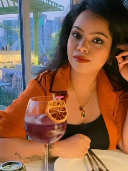 A confident and relaxed pose at a restaurant. This shows that even in a casual setting, a well-put-together outfit with a pop of color, like this orange shirt, helps you maintain a strong personal brand.