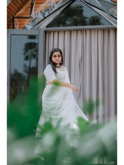 A beautiful portrait of the bride in her white lehenga, framed by greenery.