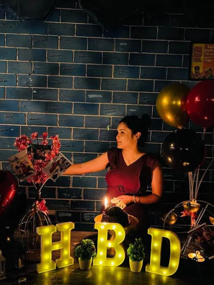 A simple yet heartfelt birthday surprise at a cafe. Against a cool blue brick wall, I set up a table with "HBD" marquee letters, a cake, and a custom photo bouquet to make her feel loved.