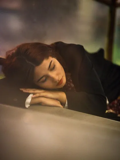 A peaceful and soft-focus portrait of a woman resting her head on her arms. The warm, gentle lighting and her closed eyes evoke a sense of calm and quiet introspection.