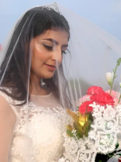 A close-up of the woman holding a bouquet, highlighting the delicate details of the white gown and veil.