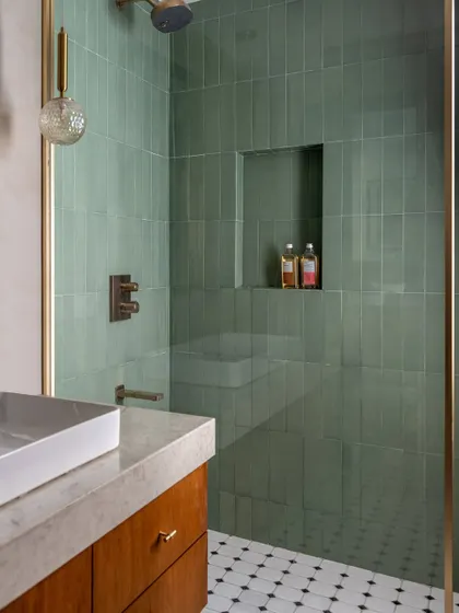 The primary bathroom features a beautiful walk-in shower with green subway tiles. The mix of materials, from the marble countertop to the wood vanity, continues the home's theme of layered elegance.