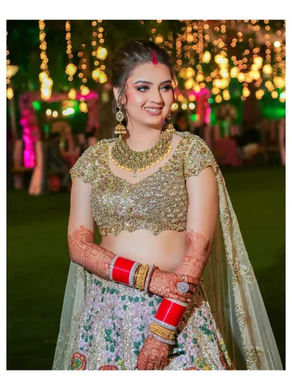 A beautiful solo portrait of the bride, smiling radiantly in her intricately embroidered reception lehenga. The bokeh from the background lights adds a magical touch.