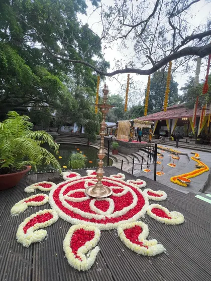 A beautiful floral rangoli made with red and white petals, with a traditional brass lamp in the center, adding to the serene and sacred ambiance.