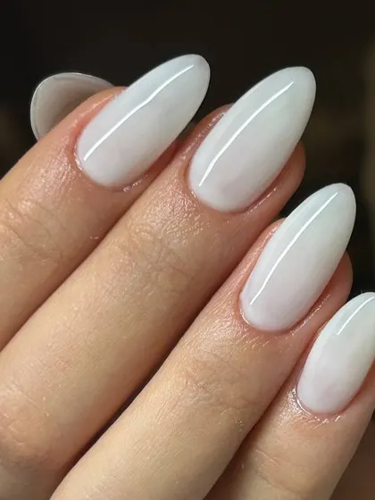 A clean, opaque white manicure on long, almond-shaped nails. The bright white and elegant shape create a striking and modern look.