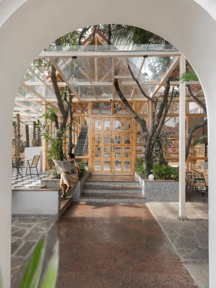 Viewed through the entrance arch, the glass-and-wood structure of the cafe is revealed, built carefully around existing trees to create a feeling of being in a forest.