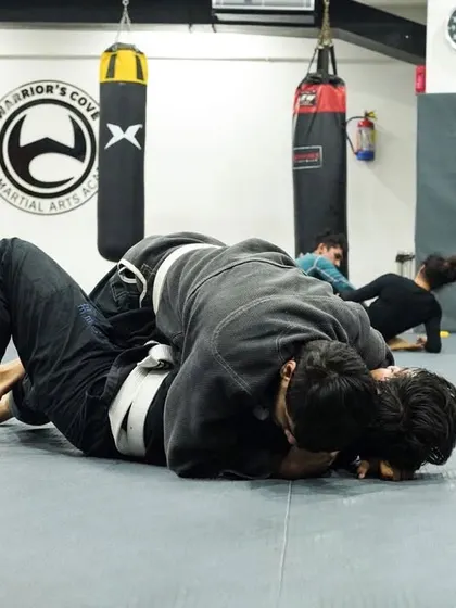 Two students in traditional white and black Gis work on passing the guard. The Gi adds a layer of complexity, teaching you to use grips to your advantage.