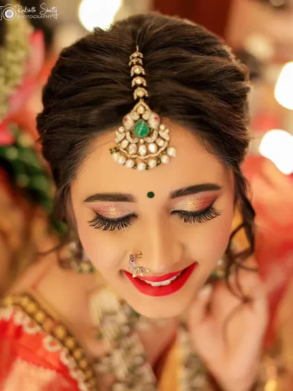 A close-up of a bride's happy and content expression. This portrait beautifully captures her flawless makeup, from the red lipstick to the shimmering eyeshadow, and her elegant maang tikka.