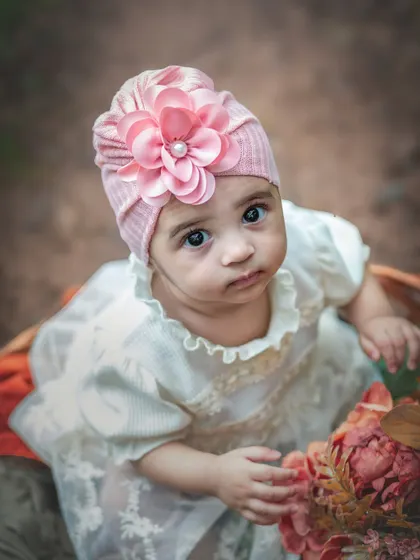 A beautiful portrait of a six-month-old baby looking directly at the camera. Her large, expressive eyes and the floral turban make this a captivating shot.