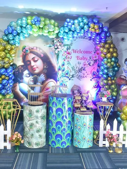 A full view of the Krishna-themed decor for a naming ceremony. The setup includes a large backdrop, character cutouts, and themed pedestals, creating a divine atmosphere.