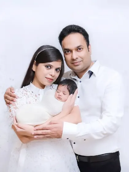 A proud new family of three. The parents hold their swaddled newborn, smiling at the camera in this classic first family portrait.