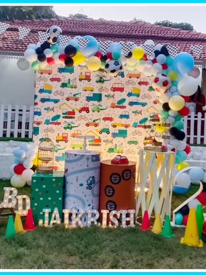An outdoor Cars-themed second birthday party. The setup includes a traffic-themed backdrop, a mini ride-on car, and traffic cone props.