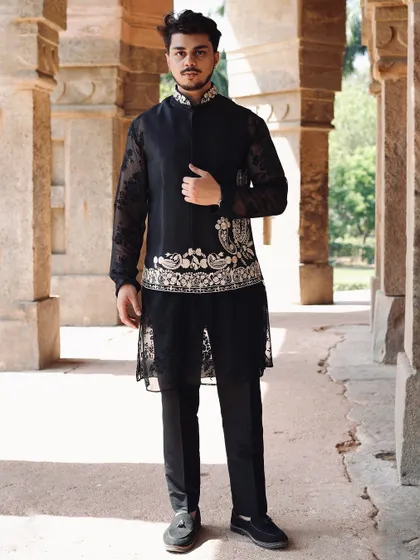This look combines a sheer black floral kurta with an embroidered asymmetric Nehru jacket. The layering of textures and patterns creates a sophisticated and modern ethnic outfit.