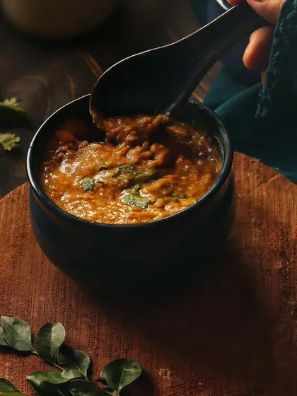 A close-up of a spoonful of Daleem being lifted from the bowl. This action shot makes the dish look dynamic and delicious, highlighting its thick, rich texture.