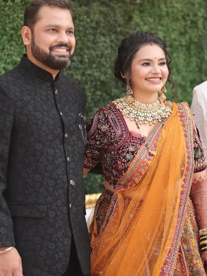 The perfect pair. Her traditional orange and maroon bridal look, complete with heavy gold jewellery, is balanced with soft, elegant makeup that enhances her natural features.