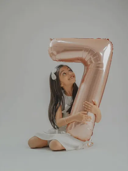 The birthday girl hugging a giant number '7' balloon. Using large props like this adds a fun and personal element to milestone birthday photos.