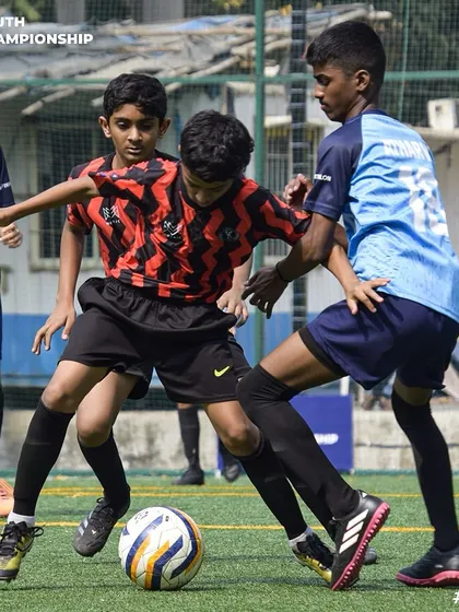 Surrounded but not beaten. Our young player skillfully protects the ball from two opponents, showcasing great composure under pressure.