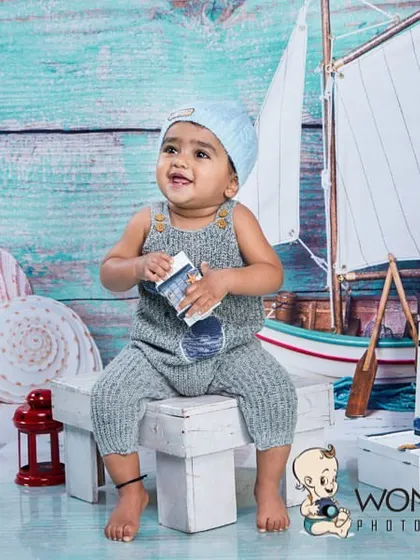 A baby boy enjoying the nautical-themed setup. The soft colors and detailed props like the sailboat and shells create a calm and charming seaside atmosphere.