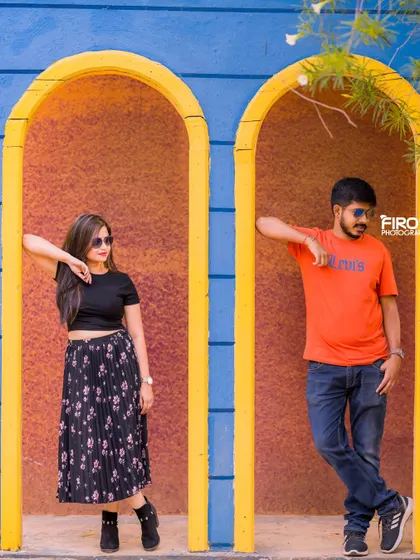 A stylish, modern pose in a colorful architectural setting. The couple's casual outfits and sunglasses give this shot a cool, editorial vibe.