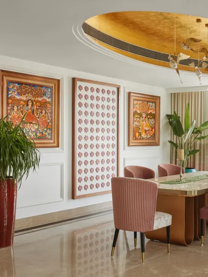 A wall of traditional Indian art adds a rich cultural layer to the dining space. The warm tones of the artwork are complemented by the pink chairs and the gold ceiling.